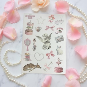 May include: A sticker sheet with pink and white illustrations of a carousel, angel, bows, and a deer. The text "The Ephemera Club" is at the top. The stickers are surrounded by pink rose petals and a pearl necklace.