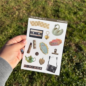 May include: A sticker sheet with various vintage-style illustrations. The designs include a cassette tape, swan, heart pendant, lipstick, mirror, cinema ticket, teapot, camera, and the word "VINTAGE". The text "FROM THE THRIFT STORE • VOL. 3" and "The Ephemera Club" are also visible.