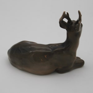 May include: A ceramic figurine of a brown deer lying down with its head turned back and antlers raised.