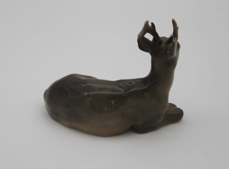 May include: A ceramic figurine of a brown deer lying down with its head turned back and antlers raised.