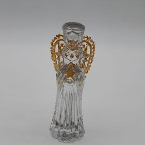 May include: A clear glass angel figurine with gold-colored accents. The angel has a star on its chest and gold-colored wings. The figurine is standing upright and has a detailed, textured design.