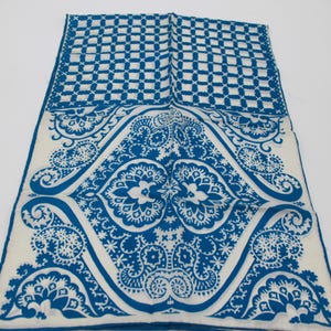 May include: A white and blue patterned textile. The top section features a blue and white checkered design. The lower section has a detailed blue floral and paisley pattern on a white background. The edges are trimmed with a blue border.