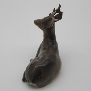 May include: A brown ceramic deer figurine with antlers, sitting on a white background.