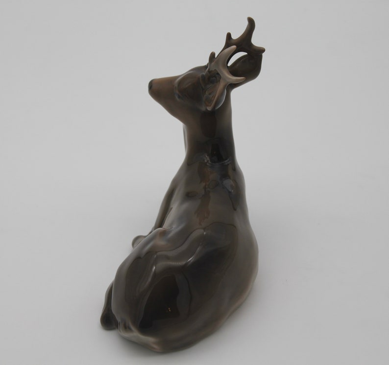 May include: A brown ceramic deer figurine with antlers, sitting on a white background.
