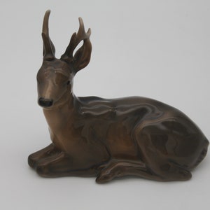 May include: A brown ceramic figurine of a deer with antlers, lying down with its head turned to the side.