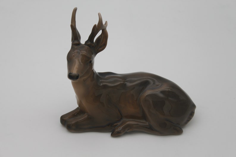 May include: A brown ceramic figurine of a deer with antlers, lying down with its head turned to the side.