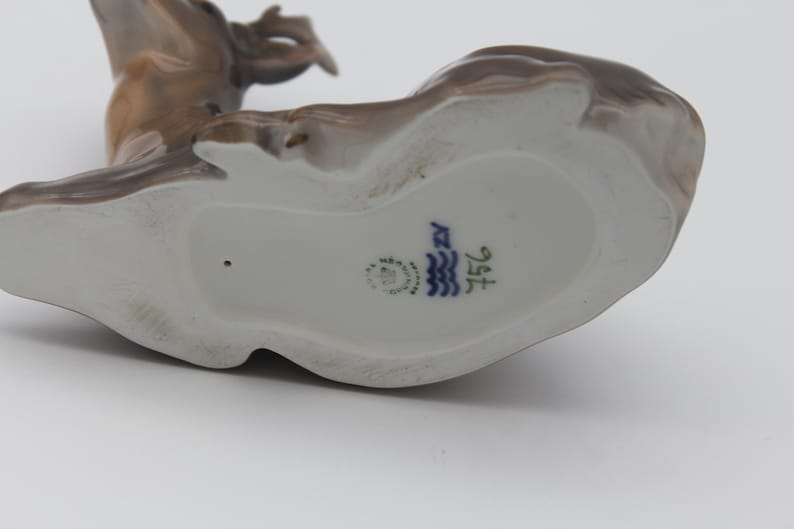 May include: The bottom of a porcelain figurine of a deer. The figurine is brown and white and has a blue and white mark on the bottom that reads "1516".
