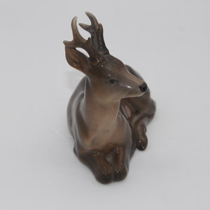 May include: A brown ceramic figurine of a deer with antlers, lying down with its head turned to the side.