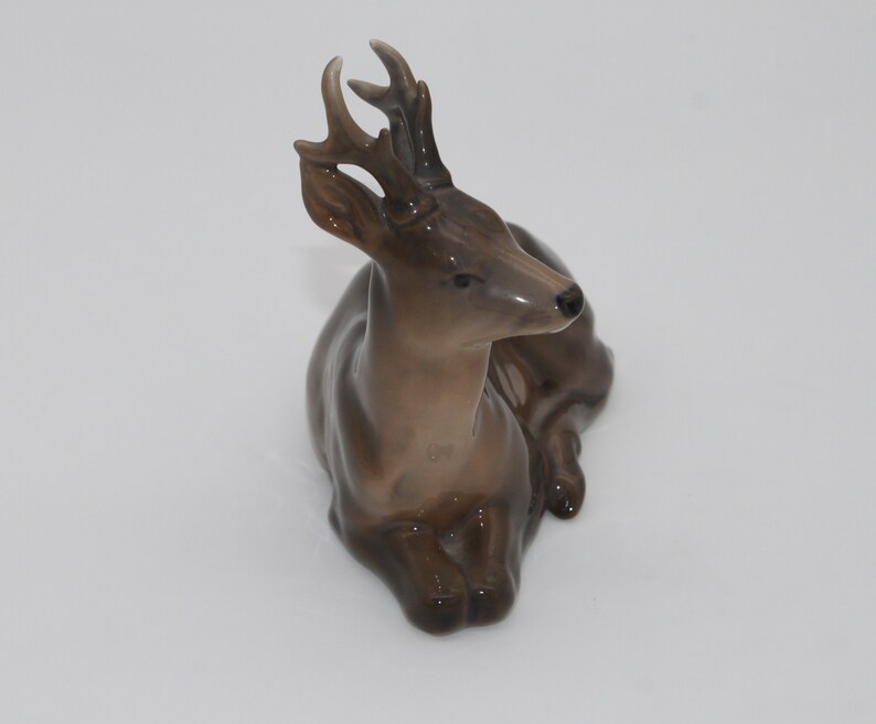 May include: A brown ceramic figurine of a deer with antlers, lying down with its head turned to the side.