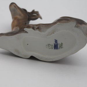 May include: A brown porcelain figurine of a deer with a white underside and a blue and white mark on the bottom that reads "1572".