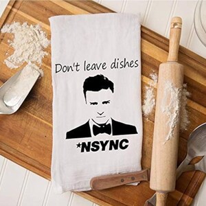May include: White kitchen towel with a black and white image of a man with the text "Don't leave dishes *NSYNC" printed on it.