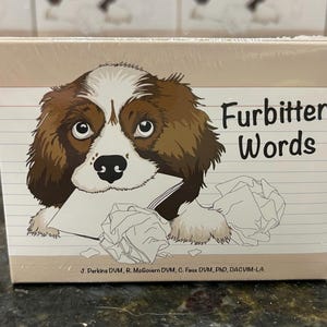 Puede incluir: Una caja de cartas de juego "Furbitten Words" con un perro de dibujos animados de pelaje marrón y blanco, sosteniendo un trozo de papel arrugado. La caja es beige con líneas negras y blancas.