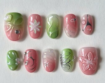 May include: Ten pink and green oval-shaped fake nails with different floral and swirl designs.