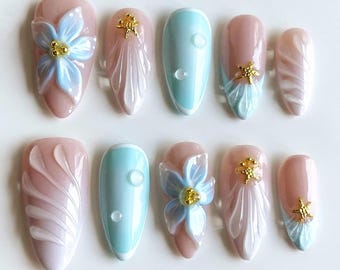 May include: Set of ten false nails with a light blue and pink color scheme. Some nails feature a 3D flower design, while others have a swirl pattern. All nails have a gold accent.