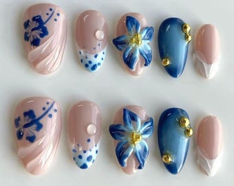 May include: Set of ten false nails with a blue and white floral design. Some nails have a light pink base, while others have a blue base. Some nails have gold accents.