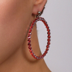 May include: A large circular hoop earring featuring a continuous row of small, faceted red beads set on a silver-toned frame. The earring attaches to the earlobe with a small silver-toned stud mechanism, creating a bold and vibrant accessory.