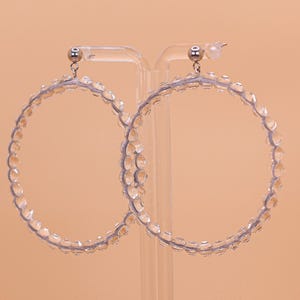 May include: A pair of large hoop earrings featuring a clear, faceted bead design. The circular hoops are constructed from a series of transparent, light-reflecting beads strung together, finished with silver-toned metal posts and earring backs.