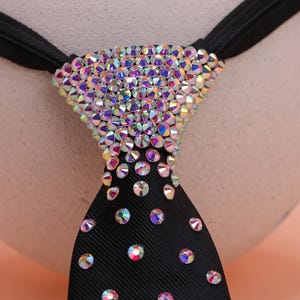 May include: A black necktie featuring a dense cluster of iridescent, multi-colored rhinestones at the knot that gradually transition into a sparse, scattered pattern of individual crystals extending down the length of the fabric.