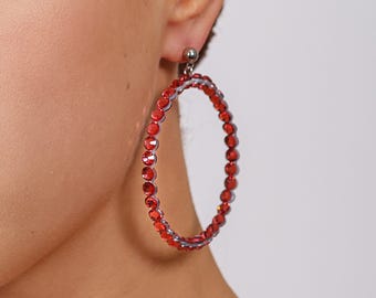 May include: A large circular hoop earring featuring a continuous row of vibrant red faceted crystals set in a metallic frame. The earring attaches to the earlobe with a small silver-toned ball stud post, creating a bold and reflective accessory.