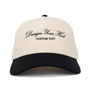 Puede incluir: Gorra de béisbol crema y negra. La gorra presenta el texto "Design Your Hat" en cursiva sobre las palabras "CUSTOM TEXT". La visera es negra.