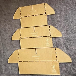 May include: Three laser-cut acrylic templates for crafting, each with a unique size: small, medium, and large. The templates are a transparent amber color, with dashed lines and cut-out sections for folding. The text "Drop Zone" is visible on each template.