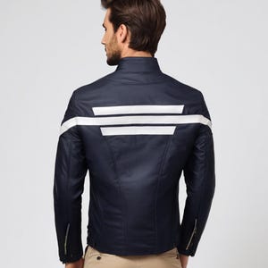 May include: Navy blue jacket with white stripes across the back and on the sleeves. The jacket has a stand-up collar and zippered sleeves. The model is wearing khaki pants. The jacket is a stylish outerwear option.