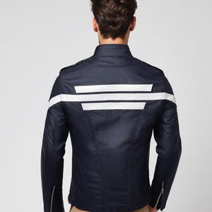 May include: Navy blue jacket with white stripes across the back and sleeves. The jacket has a stand-up collar, zipper details on the sleeves, and a tailored fit. The jacket is a stylish outerwear piece.