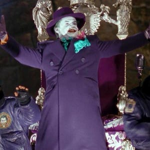 Puede incluir: Un hombre vestido como el Joker de Batman, con un abrigo morado, una corbata de lazo verde y pantalones de cuadros morados y verdes. Está de pie en un trono con un micrófono frente a él.