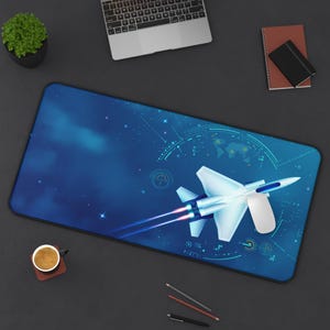 May include: A blue rectangular mouse mat with a white jet plane design and blue and red exhaust trails. The background features a starry sky and a world map graphic. A computer mouse is on the mat.