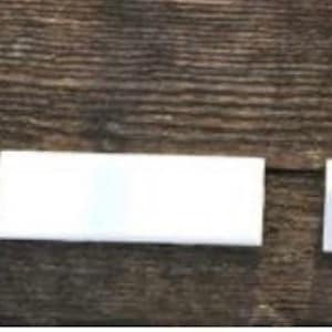 May include: Three white ceramic tiles of different sizes, arranged horizontally on a wooden surface.