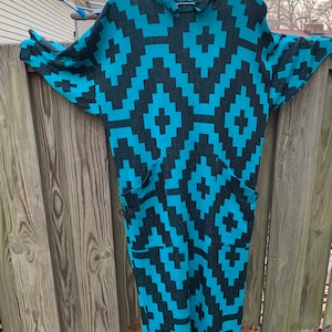 May include: A long, turquoise and black geometric patterned dress with a high neck and long sleeves. The dress has two pockets on the front.