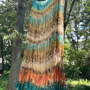 May include: A tiered maxi skirt featuring a vibrant gradient of turquoise, gold, and orange hues. The fabric displays a repeating floral and botanical print throughout, with a gathered elastic waistband and a flowing, lightweight silhouette.
