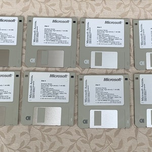 May include: A collection of sixteen 3.5-inch floppy disks, each with a gray plastic casing and a white label. The labels feature the Microsoft logo and text detailing the disk's contents. The disks are arranged in a grid pattern.