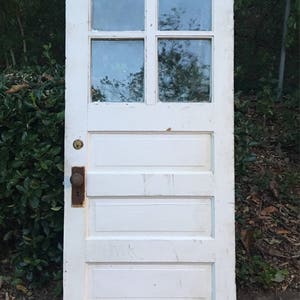 May include: A white wooden door with four glass panes and five horizontal panels. The door has a brass door knob and a keyhole.