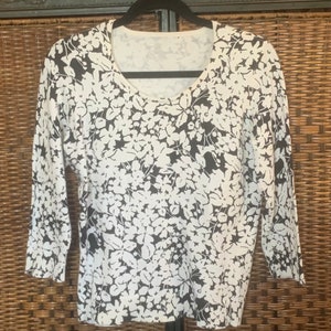 May include: White and black floral print long-sleeved sweater with a scoop neck.