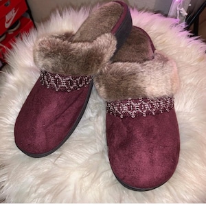 May include: A pair of burgundy faux fur lined slippers with a decorative braided trim. The slippers have a closed toe and a soft, fuzzy lining.