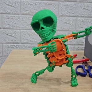 Pode incluir: Um brinquedo de esqueleto articulado verde e laranja em uma pose de dança. O esqueleto tem uma grande cabeça de caveira verde e ossos laranja.