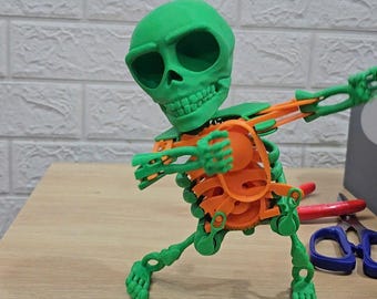 May include: A green and orange articulated skeleton toy in a dancing pose. The skeleton has a large green skull head and orange bones.
