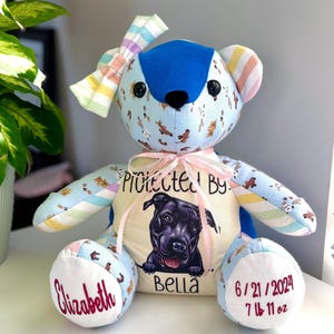 May include: A handmade teddy bear with a blue head and paws, and a light blue body patterned with brown dog illustrations. The bear has a bow and a center panel with a dog portrait and the name "Bella". The bear also has the name "Elizabeth" and the date 6/21/2024 with the weight 7 lb 11 oz.