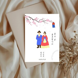 以下が含まれることがあります： 韓国の伝統的な衣装を着たカップルが描かれた結婚式の招待状。イラストには桜、提灯、韓国語のテキストが含まれています。日付2026.09.26も表示されています。