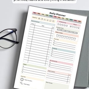 May include: A daily planner with sections for scheduling, productivity, and habit tracking. The planner includes space for time, tasks, weather, energy levels, water intake, priorities, a to-do list, and a brain dump. The text "YOUR WHOLE DAY, ONE GUIDED PAGE space for focus, priorities, habits and everything in between" is at the top.