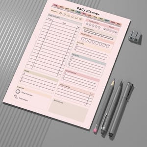 May include: A pink Daily Planner sheet with sections for scheduling, tasks, and tracking habits. Includes a habit tracker, water intake, and mood tracker. Three gray pens and a pencil sharpener are next to the planner.