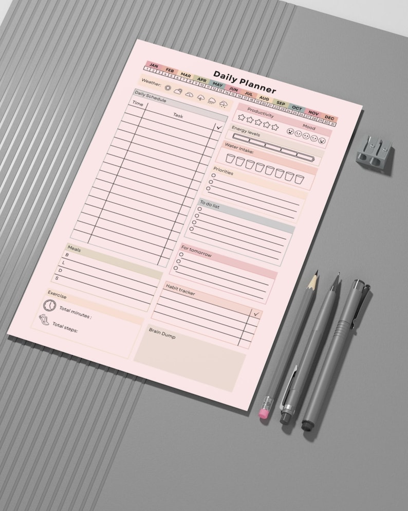 May include: A pink Daily Planner sheet with sections for scheduling, tasks, and tracking habits. Includes a habit tracker, water intake, and mood tracker. Three gray pens and a pencil sharpener are next to the planner.