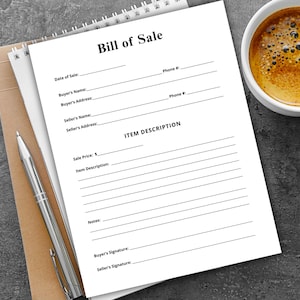 May include: A white Bill of Sale form with a spiral binding, lying on a brown notepad. A silver pen rests on the notepad. A cup of coffee sits to the right. The form includes fields for buyer and seller information.