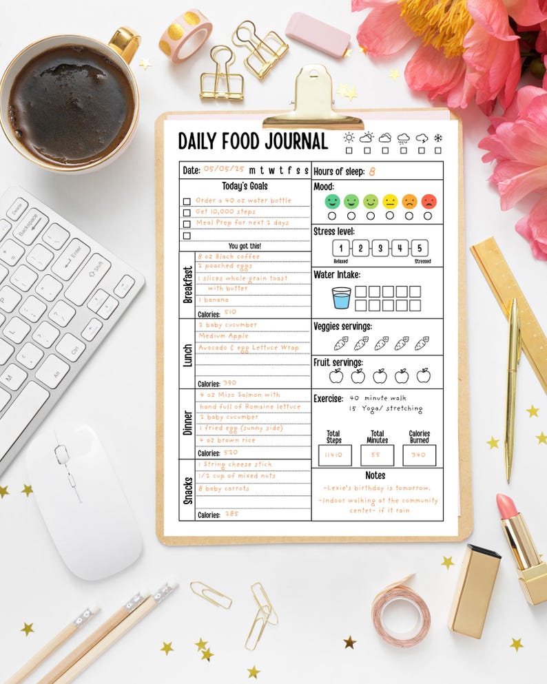 May include: A clipboard with a "Daily Food Journal" form, a cup of coffee, a computer mouse, and a keyboard. The form includes sections for goals, mood, water intake, and meal tracking. Gold paper clips, pencils, and a lipstick are also visible.