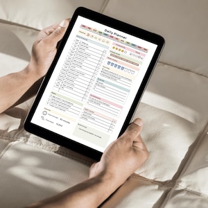May include: A black tablet displaying a "Daily Planner" template, held by hands. The planner features sections for daily schedules, to-do lists, and notes, with colorful headers and checkboxes. The tablet is on a light-colored surface.