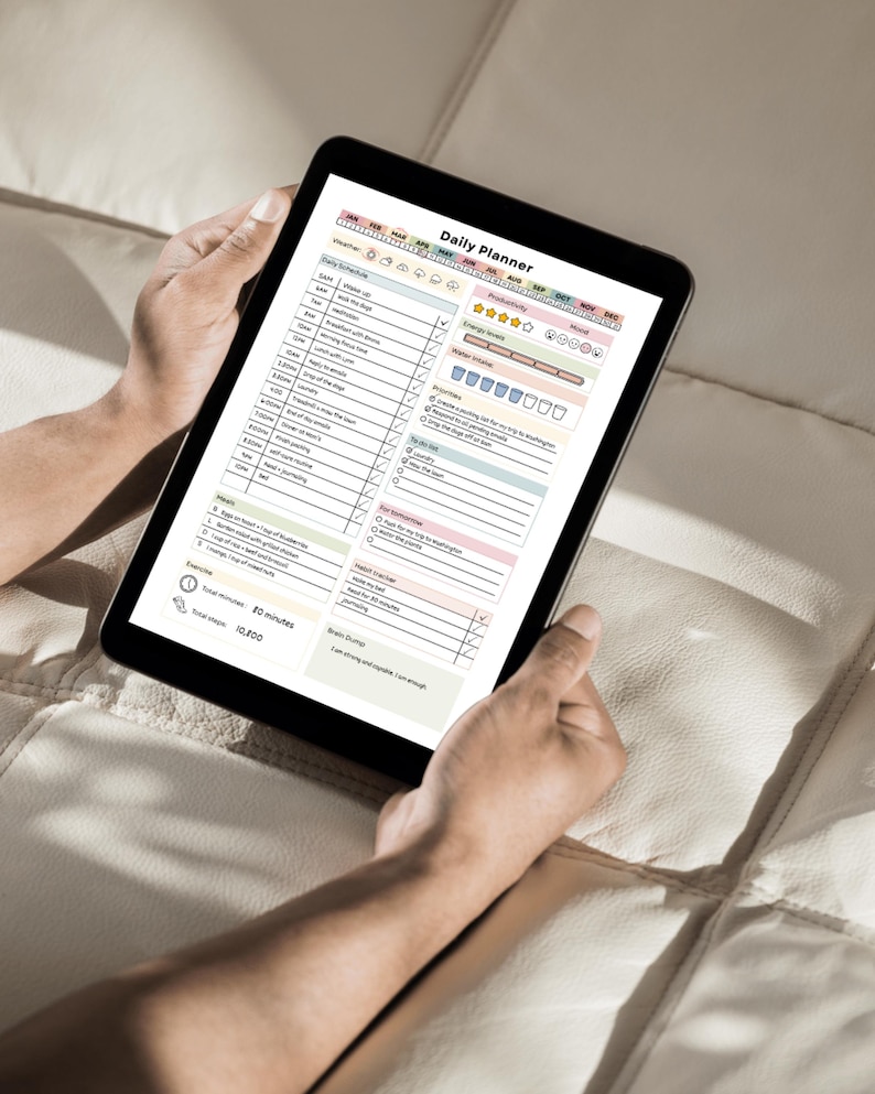 May include: A black tablet displaying a "Daily Planner" template, held by hands. The planner features sections for daily schedules, to-do lists, and notes, with colorful headers and checkboxes. The tablet is on a light-colored surface.