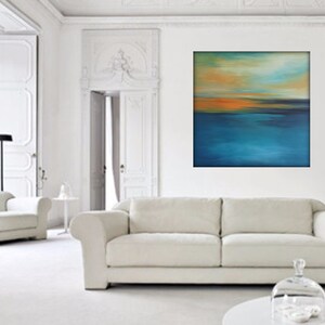 May include: A white couch with a white armchair in a white room with a large abstract painting of a blue and orange sunset over water.