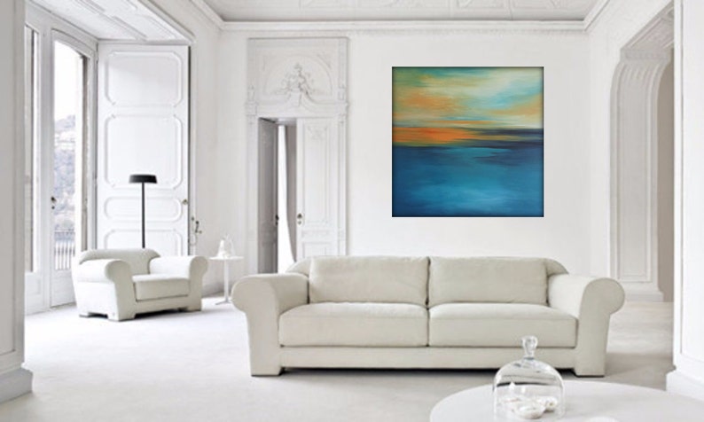 May include: A white couch with a white armchair in a white room with a large abstract painting of a blue and orange sunset over water.