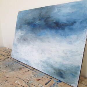 Op de afbeelding: Abstract schilderij op canvas met een blauw en wit kleurenschema. Het schilderij heeft een verloop van blauwe tinten, die naar beneden toe overgaan in een lichter wit. De penseelstreken zijn zichtbaar en cre&euml;ren een textuur effect.